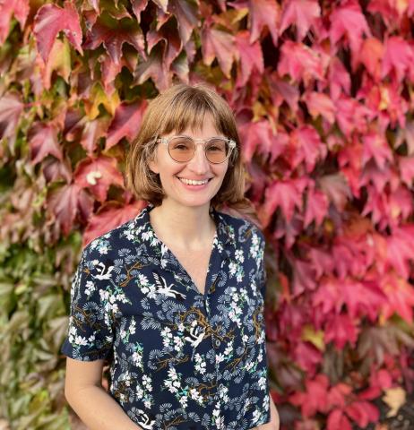 Faculty member standing outside in front of a wall covered with fall leaves