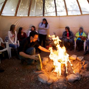 group of people sitting on chairs around a fire in the tipi (teepee) at Trent University