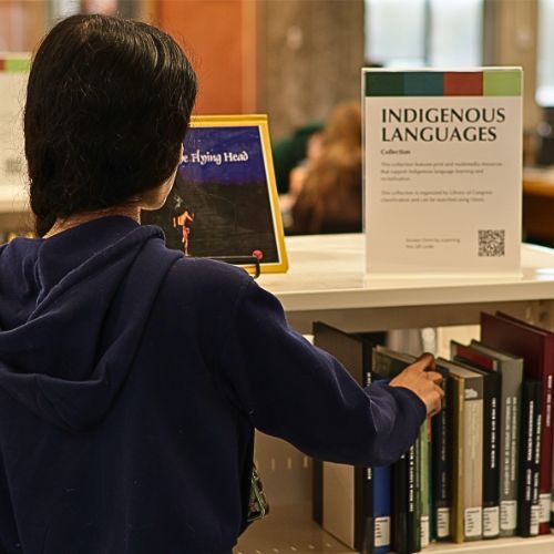 A student selects a book off a shelf from the Indigenous Language Collection in the Bata Library at Trent University