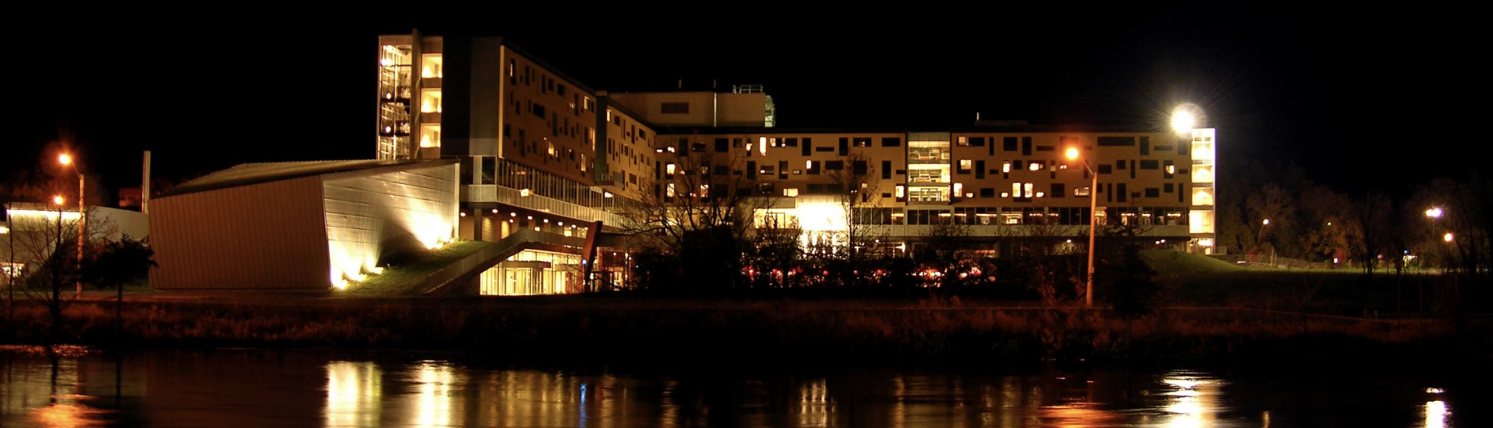 Gzowski College at night with lights reflecting off the Otonabee River
