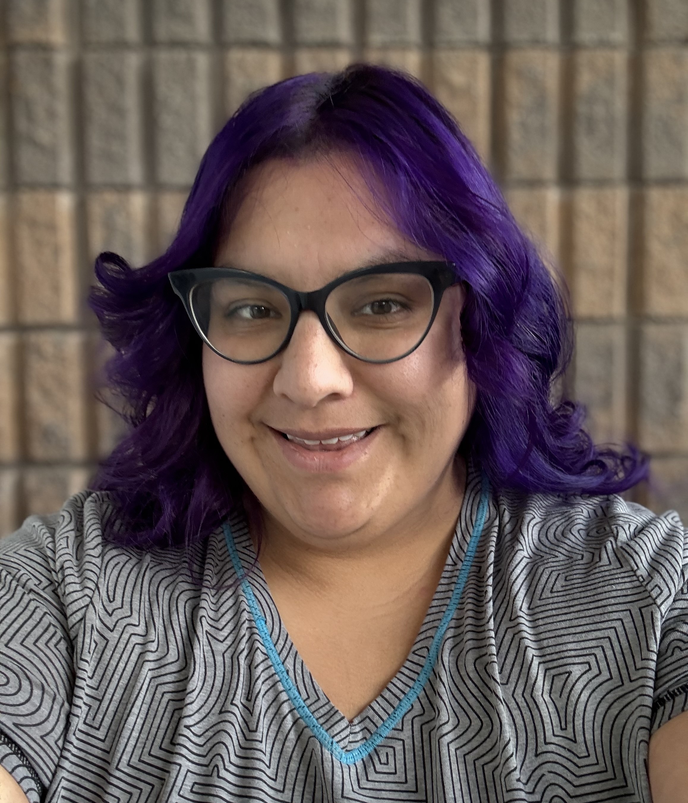 Student with purple hair and black rimmed glasses smiling.