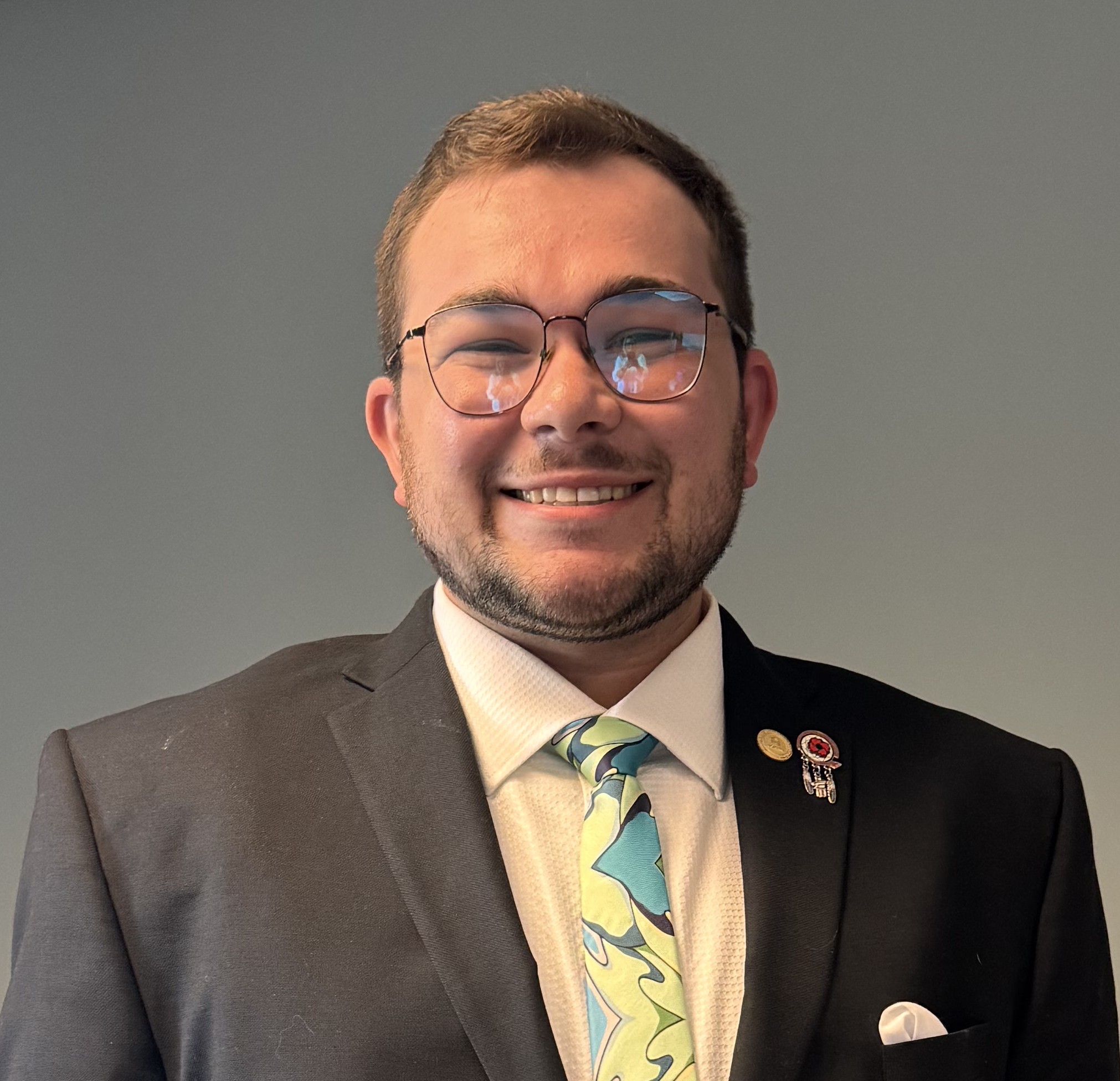 Smiling man with glasses, brown hair with suit jacket and light green tie.