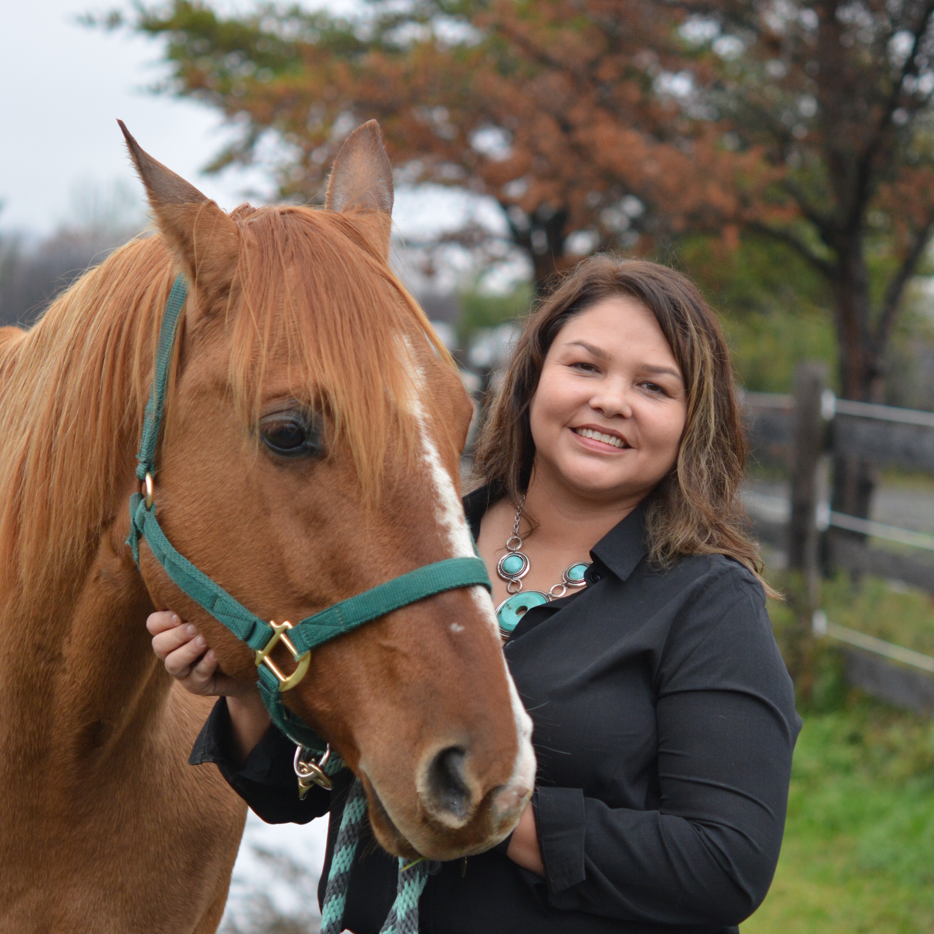 Woman smiling and standing with rusty brown coloured horse.