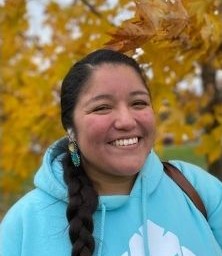 Woman with long dark braid smiling in a turquoise sweatshirt