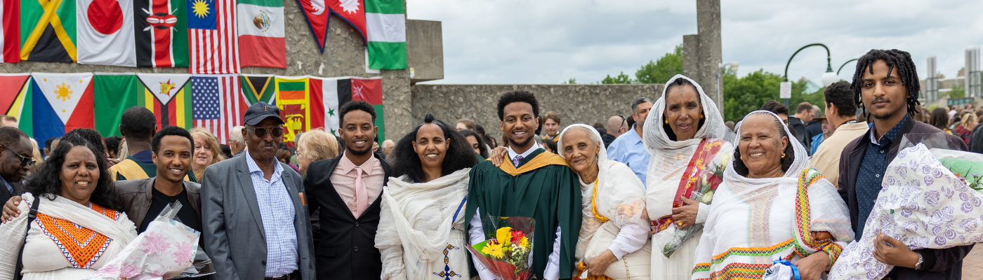 A family standing on a platform in front of a crowd and flags of various countries