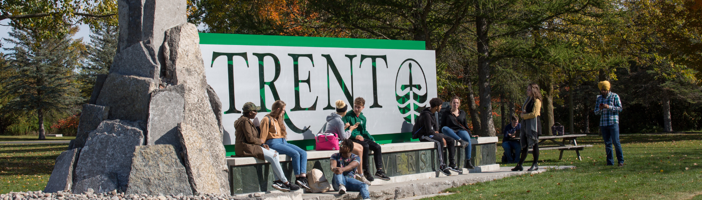 A group of students sitting in front of the main Trent University sign