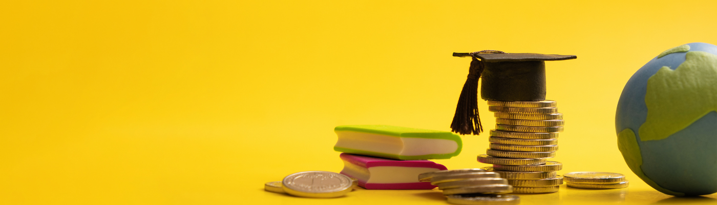 Stack of coins next to a book, graduation cap, and globe