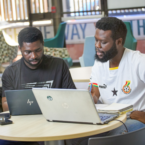 Two students using laptops at a shared table