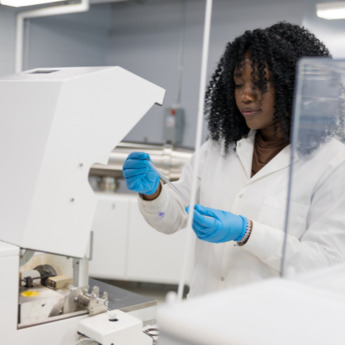 A student in a lab coat analyses a sample using lab equipment