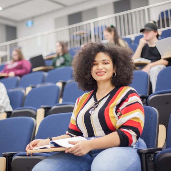 Student in lecture hall, smiling at camera.