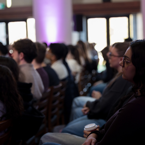 A row in a crowd of people watch a lecture in a dimly lit room with lighting effects
