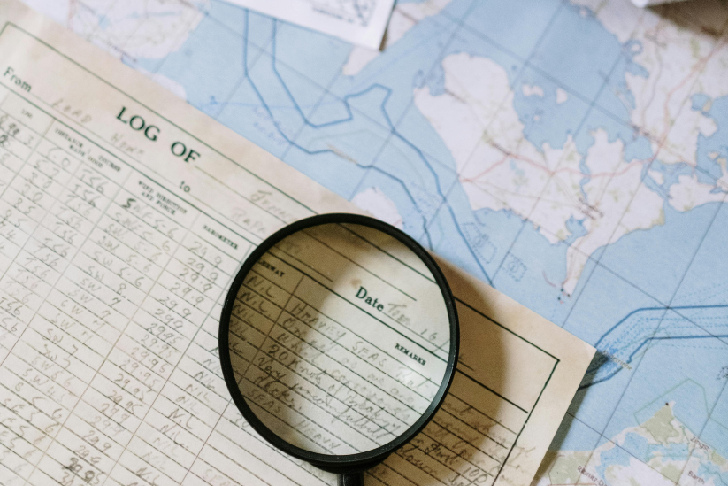 A magnifying glass highlighting part of a log book over a background of maps.