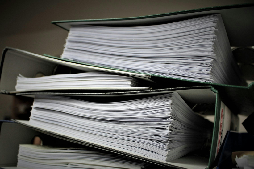 A stack of overflowing binders packed with sheets of white paper.