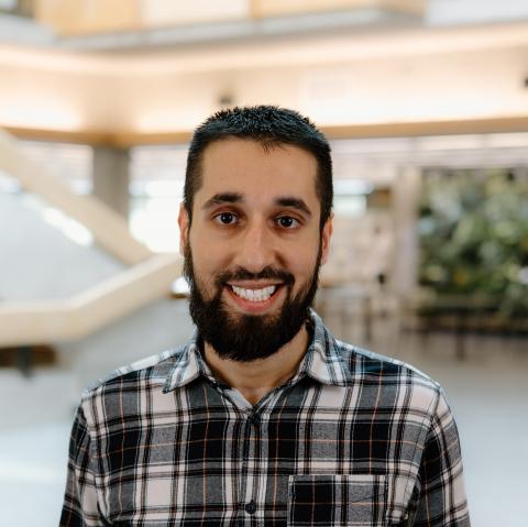 A man with a beard, dressed in a plaid shirt, smiles in the Bata Library atrium.