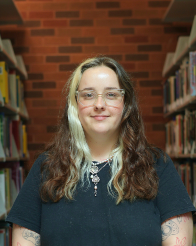 Library staff member standing in a library aisle between bookshelves.