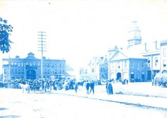 A photograph of a street scene in hues of blue, with buildings, people, and a horse and buggy