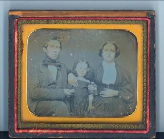 A black and whitte photograph of a man, woman, and child, inside a frame with yellow, goldish and red matting.