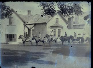 Black and white image of people on horses in front of a white building. There is some bluish discolouration on the lower right quadrant.