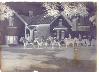 A black and white negative image of people on horses outside a building. There is some yellowish discolouration on the photograph