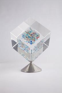 Glass sculpture in shape of cube that is clear around edges and multicoloured in the center.