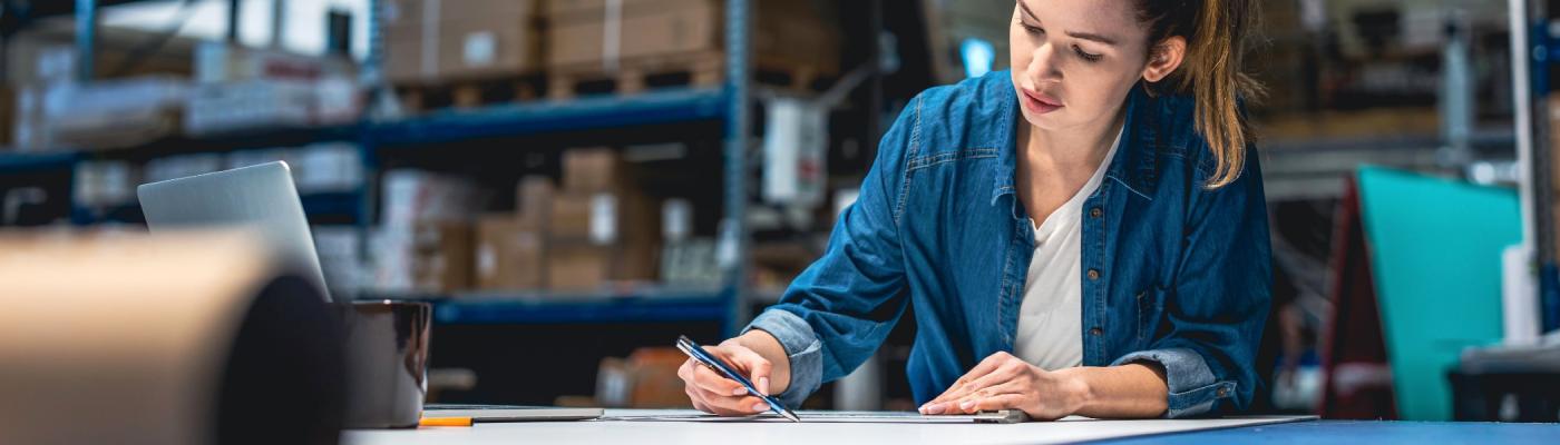 A woman working on a blueprint in a warehouse.