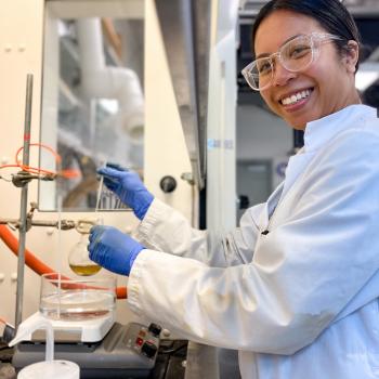 student working in fumehood smiling at camera