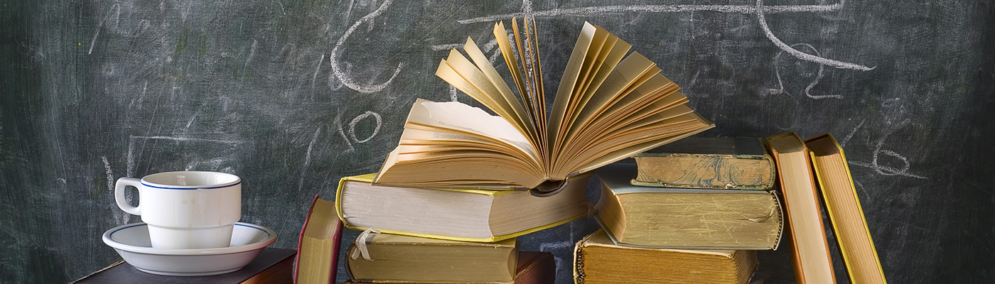 A stack of books in front of a chalkboard with a coffee cup.