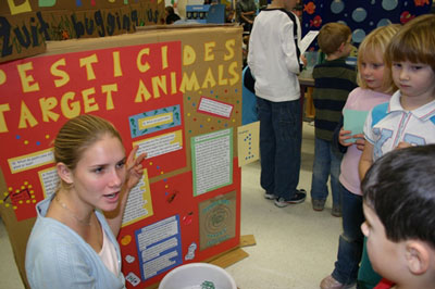 Photo 1: Trent student Laura Albrecht shows three Grade 1 students at Millbrook South Cavan Public School her exhibit on Pesticides.