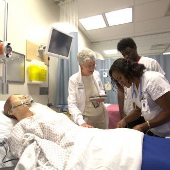 Two students and one nursing professor working over a mannikin in a nursing lab