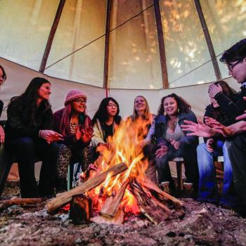 students seated around a fire pit inside a Tepee