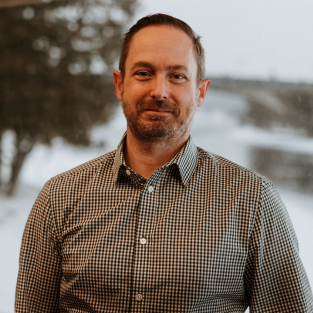 Jamie Elcombe smiling in a plaid shirt