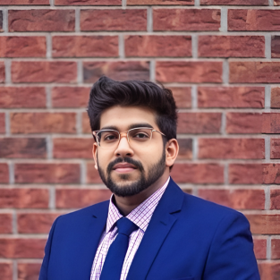 Photo of Rahul smiling in a suit in front of a brick wall