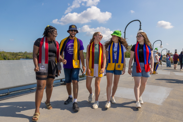 Group of five students wearing coloured scarves walk across bridge