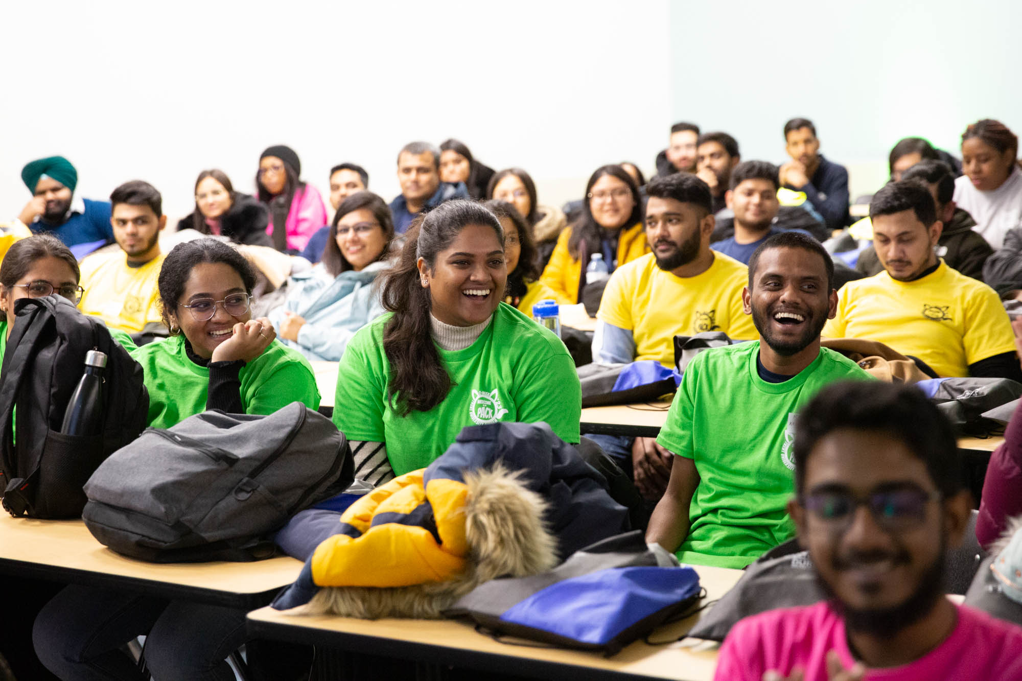 A classroom is full of students wearing colourful trent orientation tshirts with the front row of students smiling.