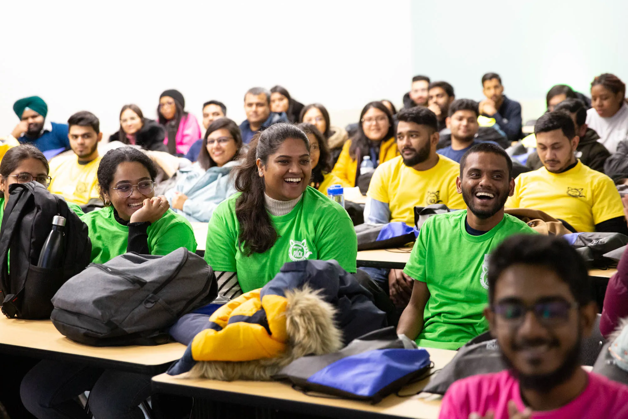 A classroom is full of students wearing colourful trent orientation tshirts with the front row of students smiling.