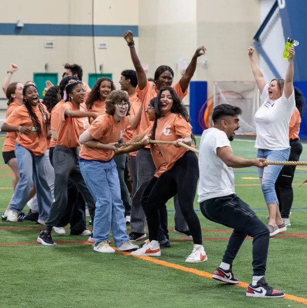 A team of diverse ethnicity students is playing tug of war and cheering their teammates on.