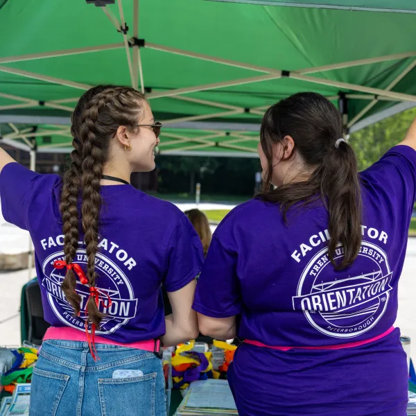Two students facing the the back standing beside each other smiling.