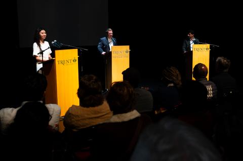 3 people speaking in front of a crowd