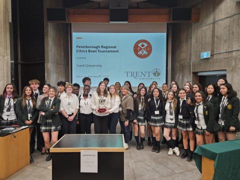 A group photo of competing teams from the 2025 Peterborough Regional Ethics Bowl Tournament. The winning team stands front and centre holding the championship trophey