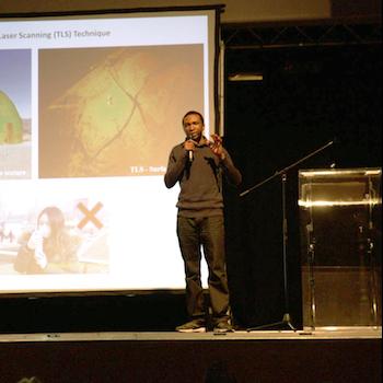 A presenter standing in front of a big screen giving a talk