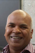 Balaji Subramanian standing in front of a blackboard smiling