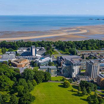 Aerial view of Swansea University, with buildings and a green wooded area right on the coast.