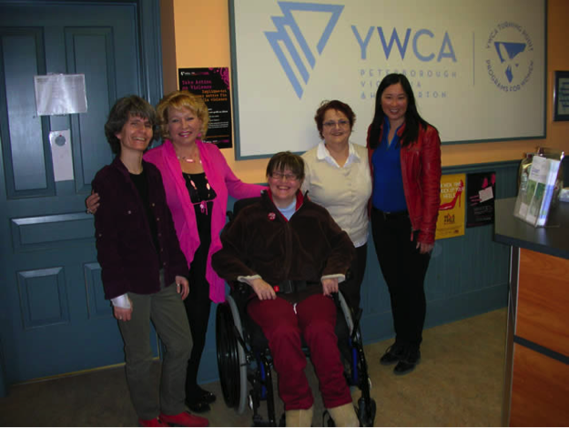 5 Professors pose in front of a poster at YWCA