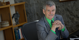 Dr. Leo Groarke smiling at the camera in his office, wearing a blue suit and tie