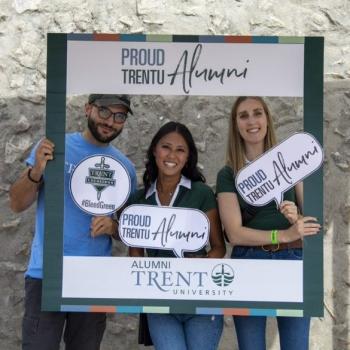 Three Trent Alumni posing for a photo with a Trent Alumni frame.