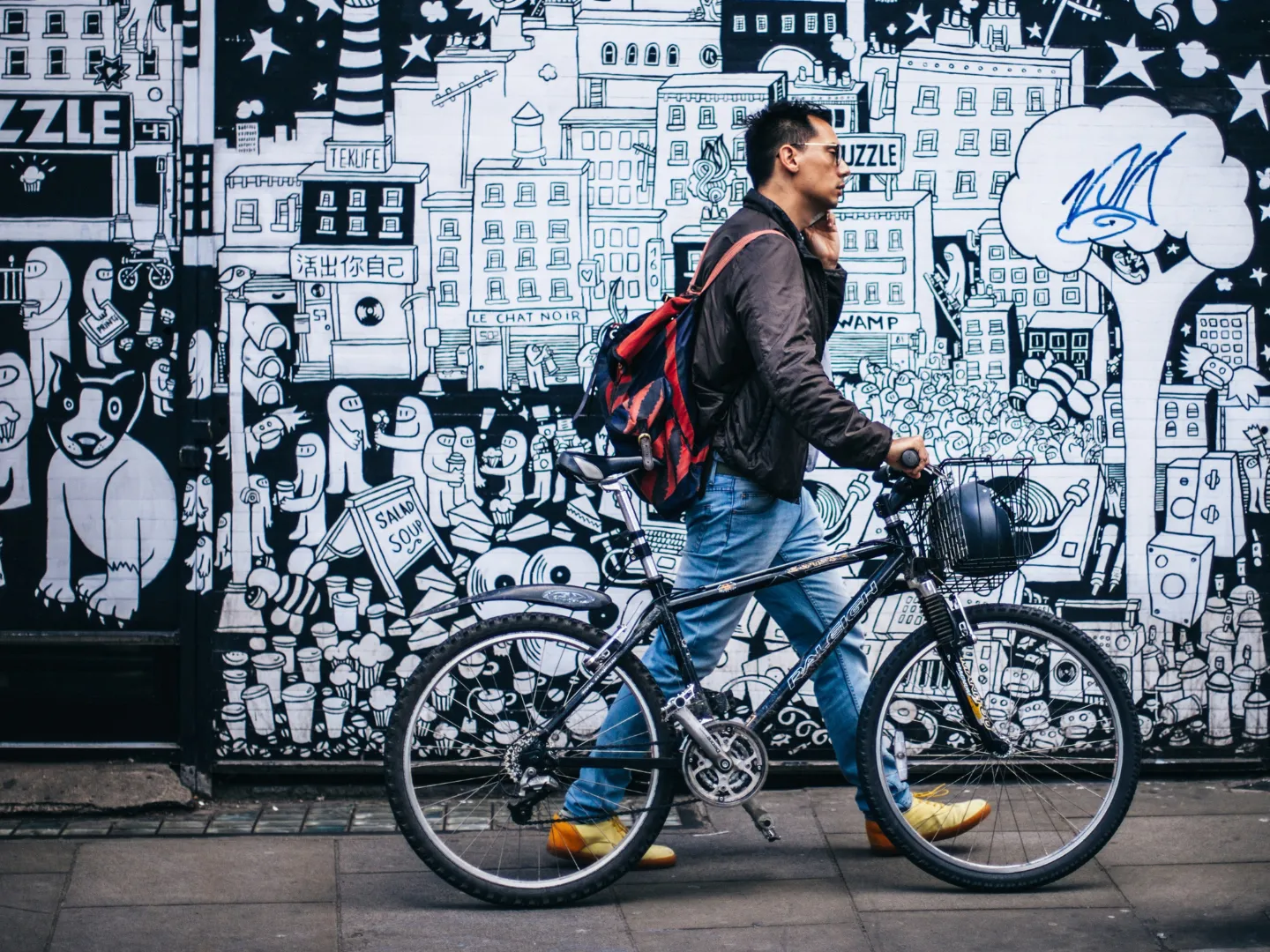 Person pushing bicycle past a mural.