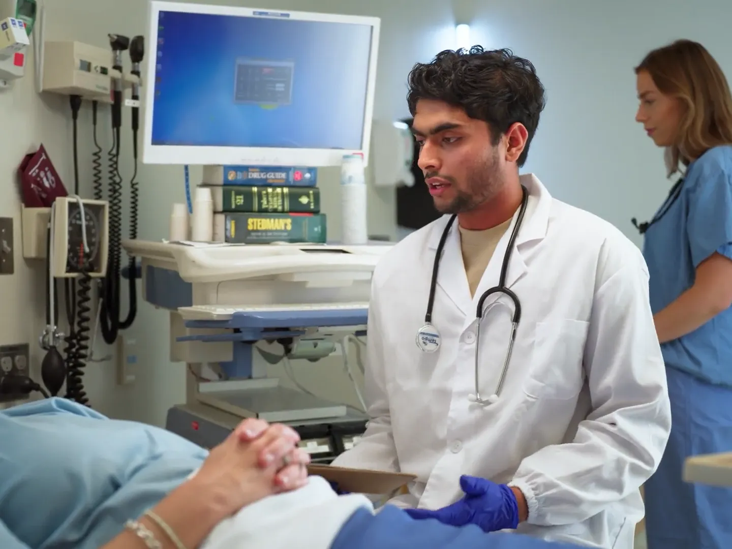 Trent student doctor and nurse talking to patient in hospital room.