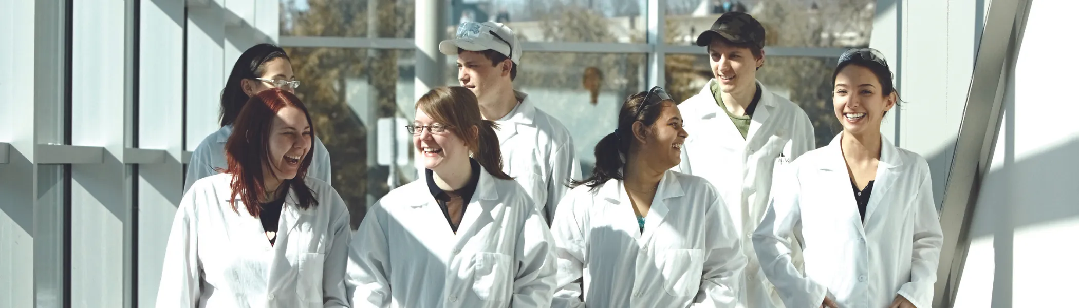 A group of Trent University science students, wearing lab coats, walking down the chemical science building hallway.