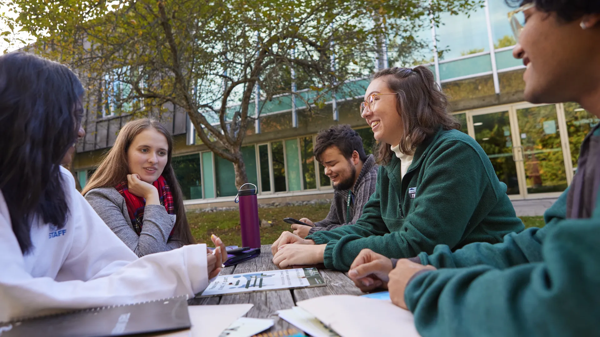 A group of Trent University students sitting at a picnic table, with their books, talking. 