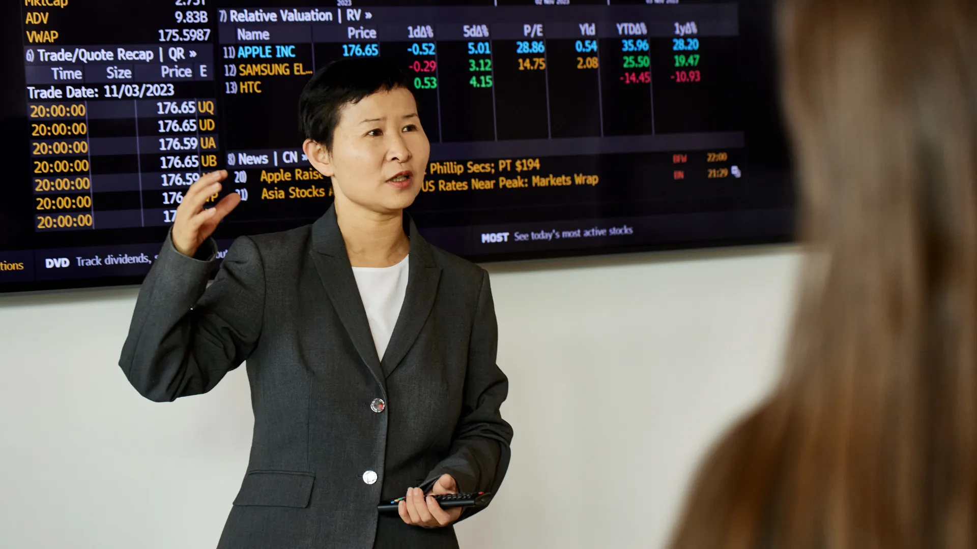 Trent University professor teaching in front of tv showing stock prices.